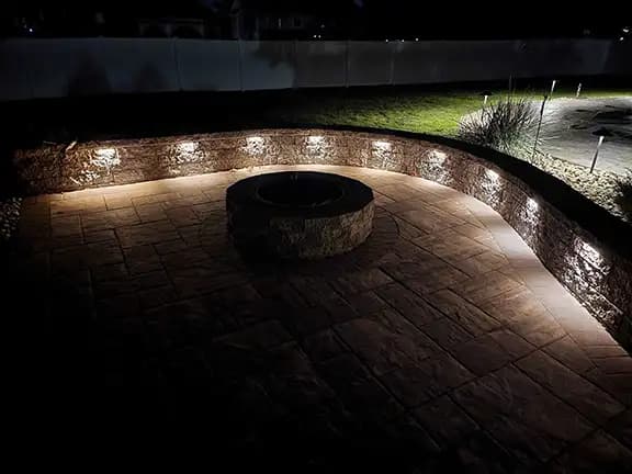 Fire pit patio area with stone wall and professional uplighting