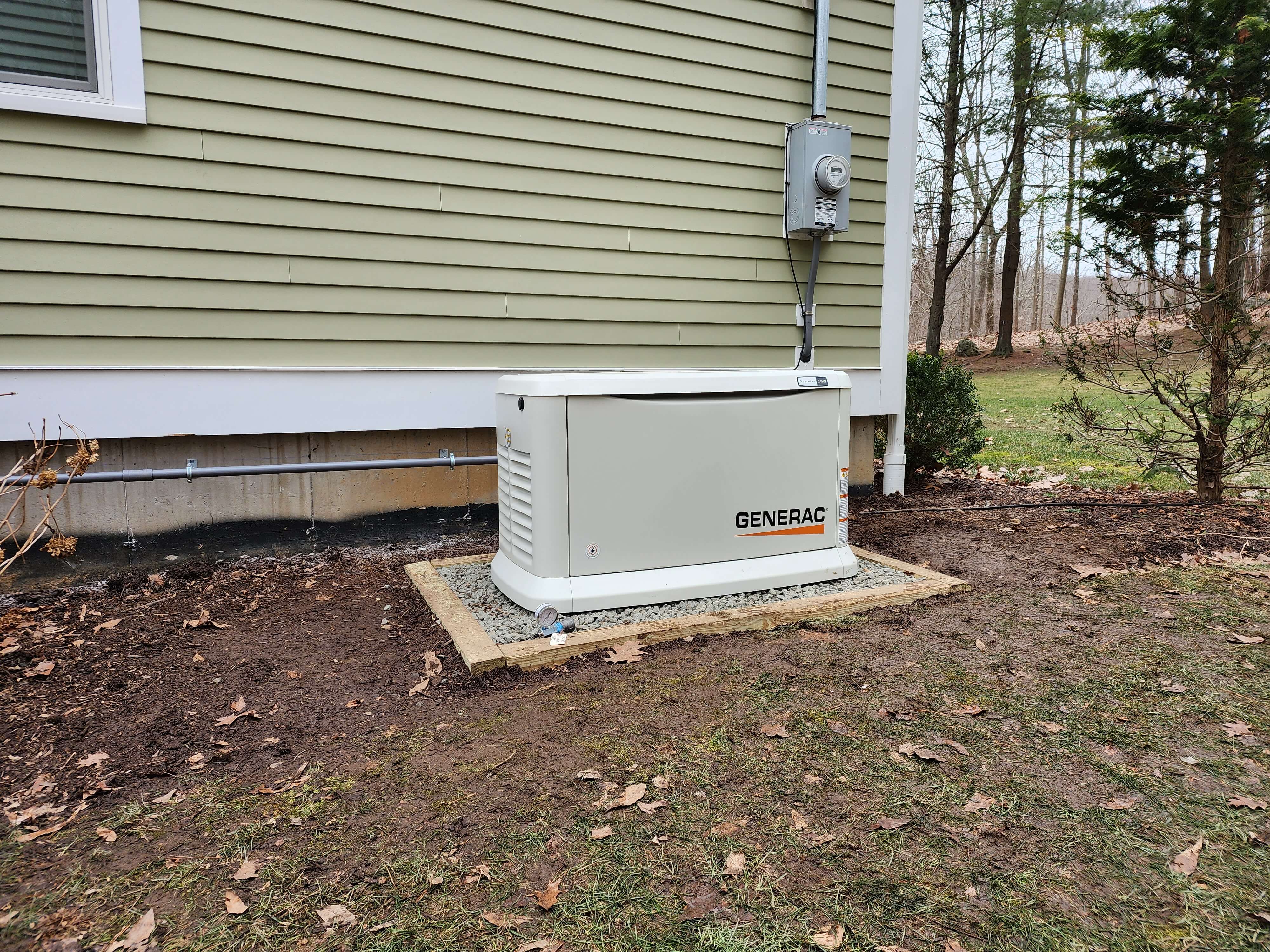 Generac generator on gravel pad next to green-sided home