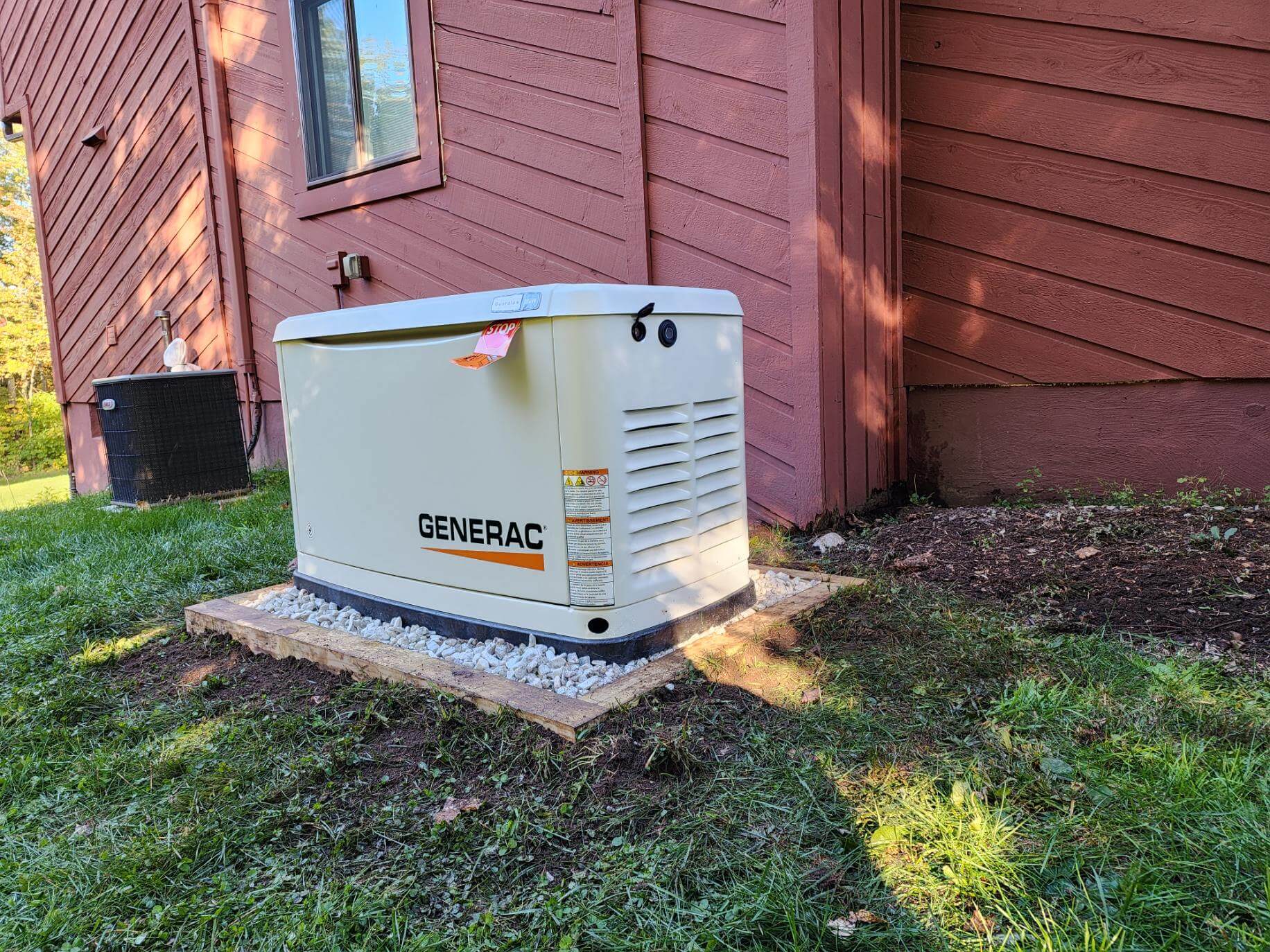 Generac generator on gravel pad next to red-sided home