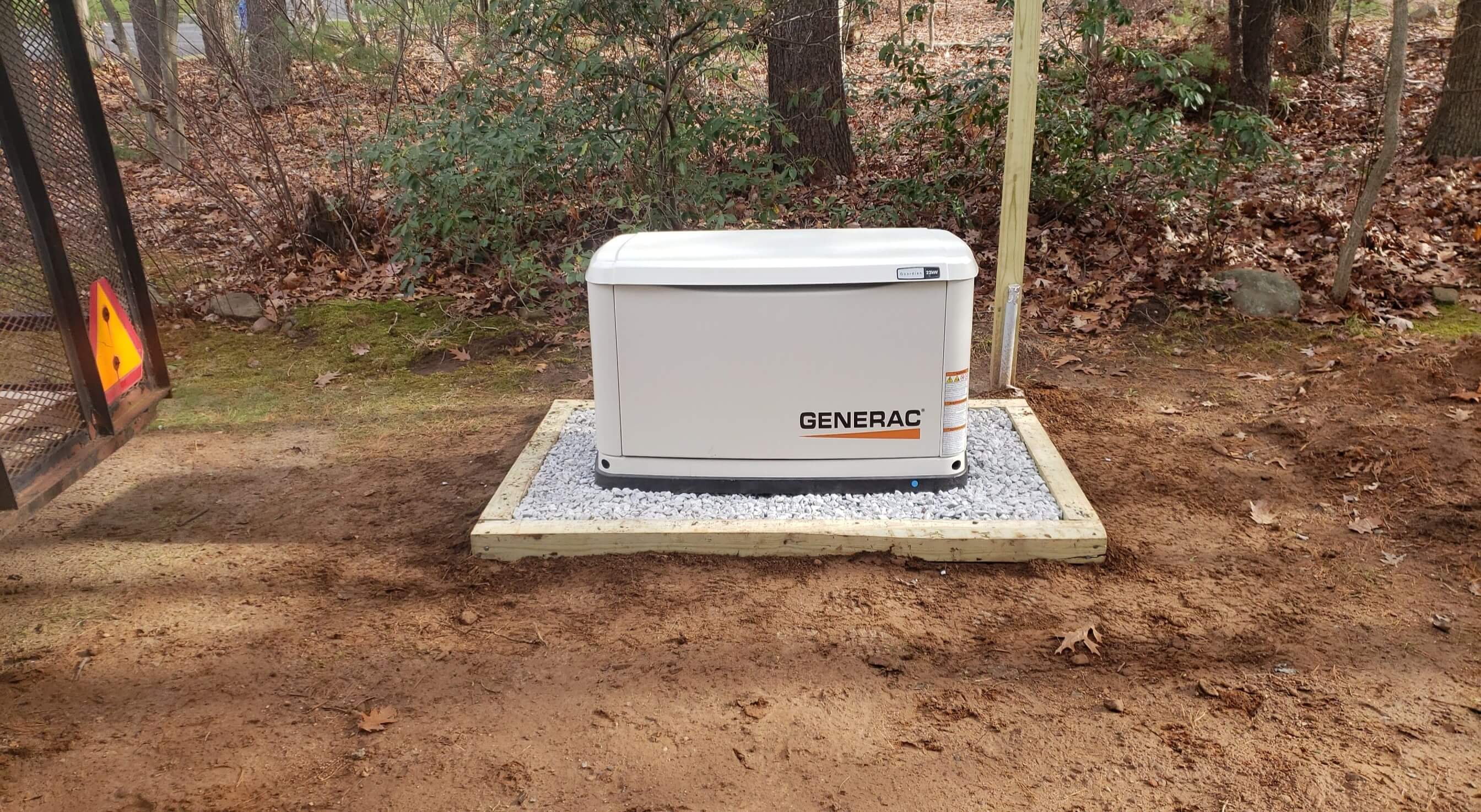 Generac generator on white gravel pad in wooded backyard