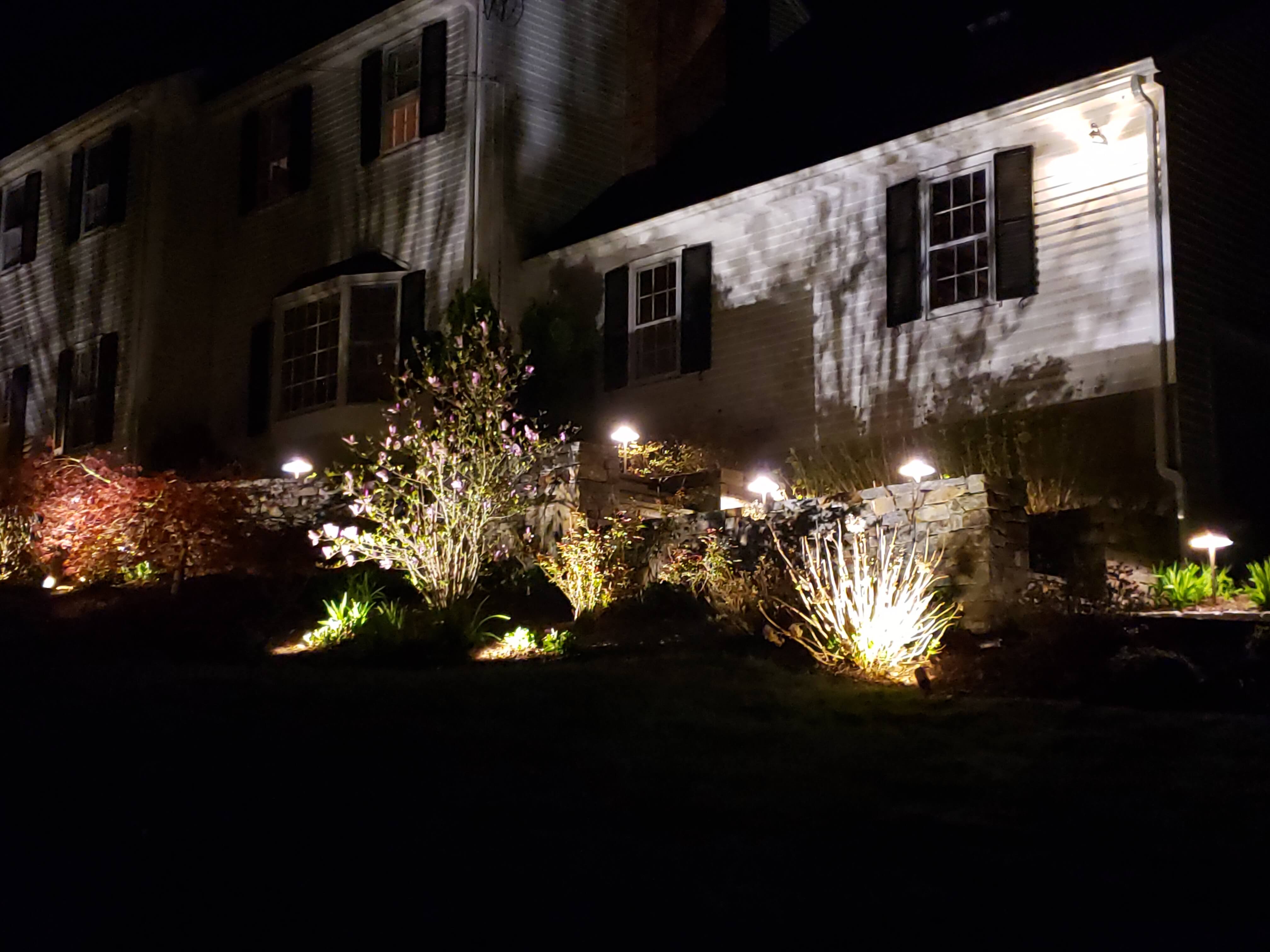 Colonial home at night with dramatic landscape uplighting and path lights