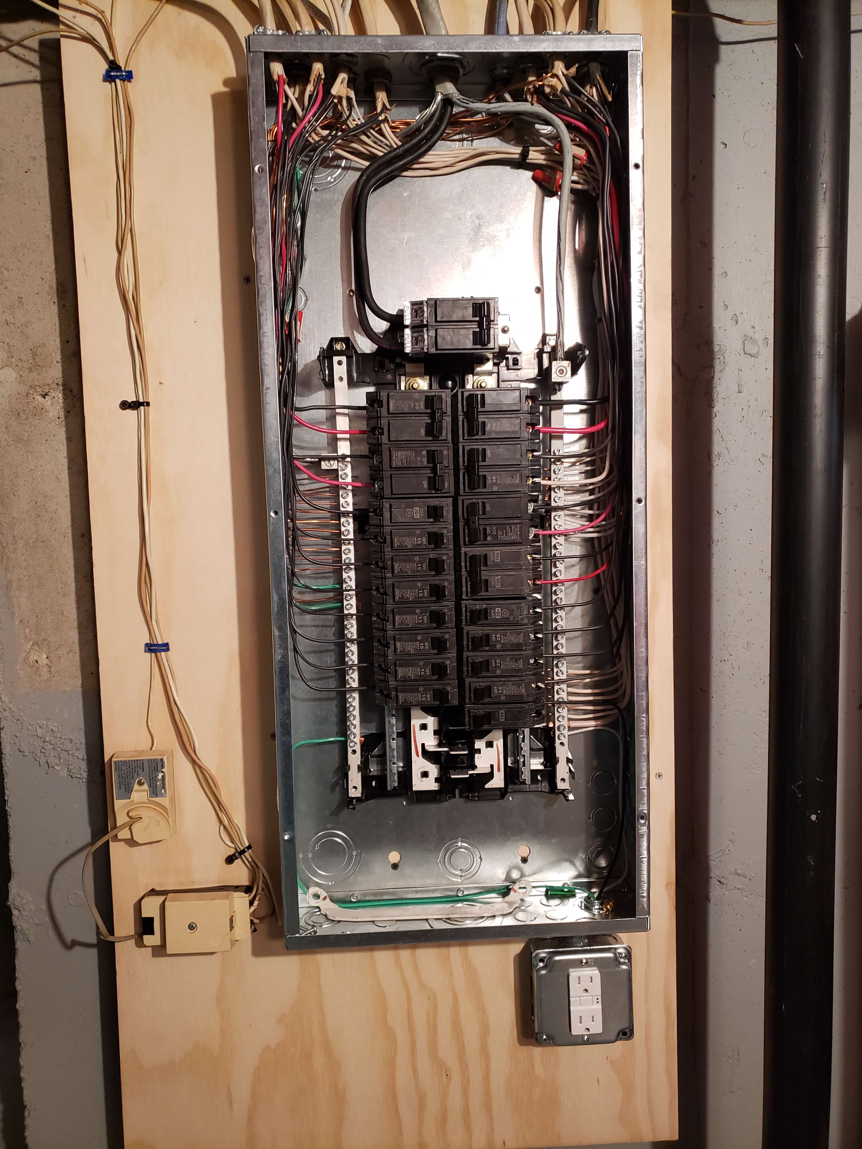 Electrical panel on plywood backboard in basement with GFCI outlet