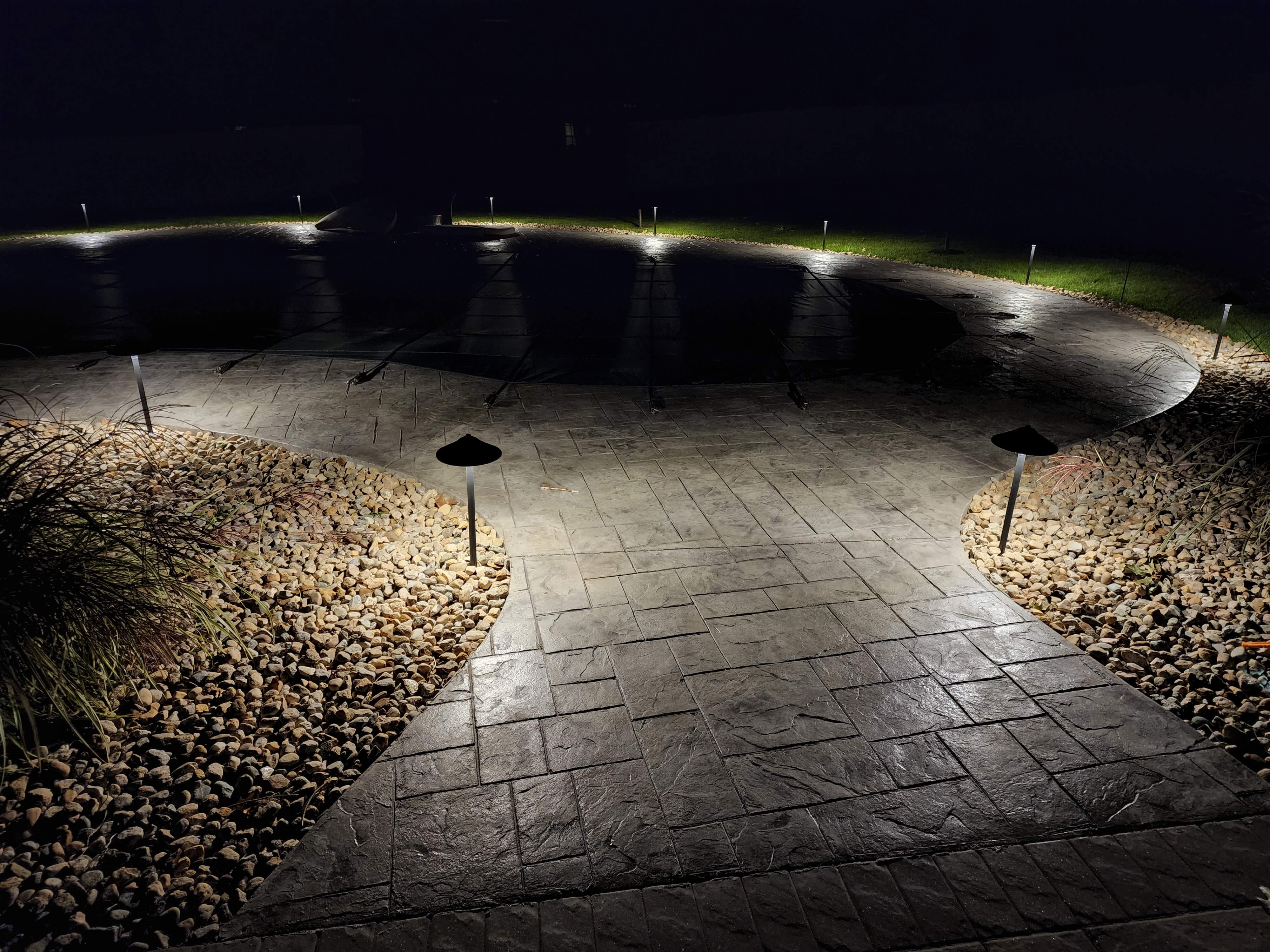 Pool patio at night with pathway lighting around covered pool